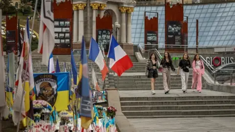Reuters People pass by a makeshift memorial to fallen Ukrainian defenders at Independence Square, where there are flags of other countries, including France, in Kyiv