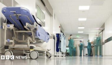An image of a hospital corridor with a stretcher at the left, and staff wearing green surgical uniforms