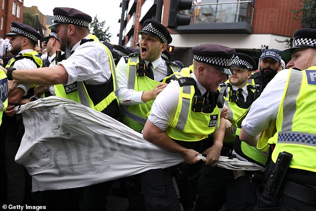 Police attempt to make their way through a fabric protest sign as they clash with an anti-fascist group in north Islington