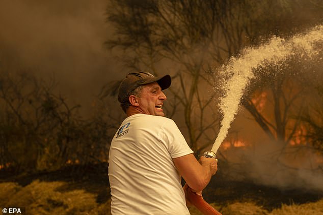 A resident holds a water hose as he tries to extinguish a wildfire in Lamas, Cualedro municipality, Galicia region, Spain