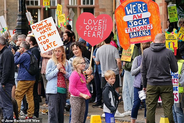 People holding signs take part in a counter protest against an Abolish Asylum System protest outside the Radisson Hotel in Perth. One sign reads: 'Don't chose hate it's not too late'