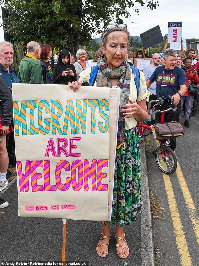 A counter protester holds a sign reading 'migrants are welcome no room for hate' in Mold, North Wales