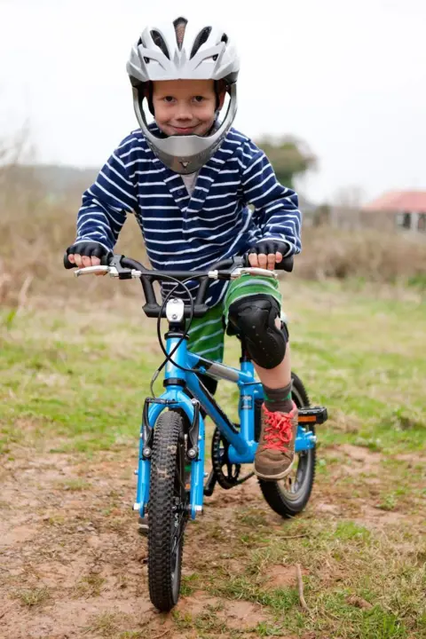Family photo A young Ioan Hepburn in shorts and a striped long-sleeved top. He's stood on a blue bike, wearing knee pads and a full-face helmet. 