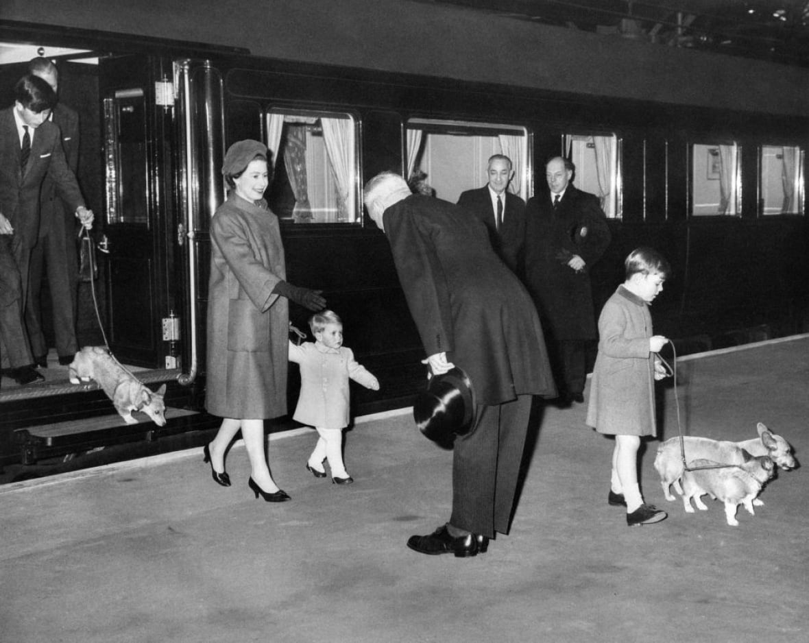 A teenager steps off a train with a dog on a leash while another adult and two children walk ahead with other dogs.