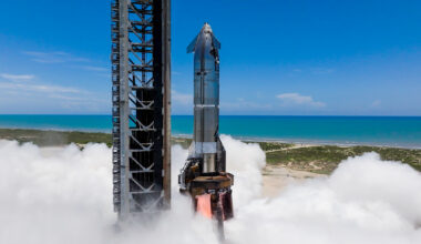 a silver rocket fires one of its engines on a seaside launch pad