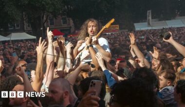 A member of the band Idles is held aloft by the crowd as he plays his guitar during a concert in Queen Square in Bristol. Thousands of people along with food and drink stalls are visible in the background