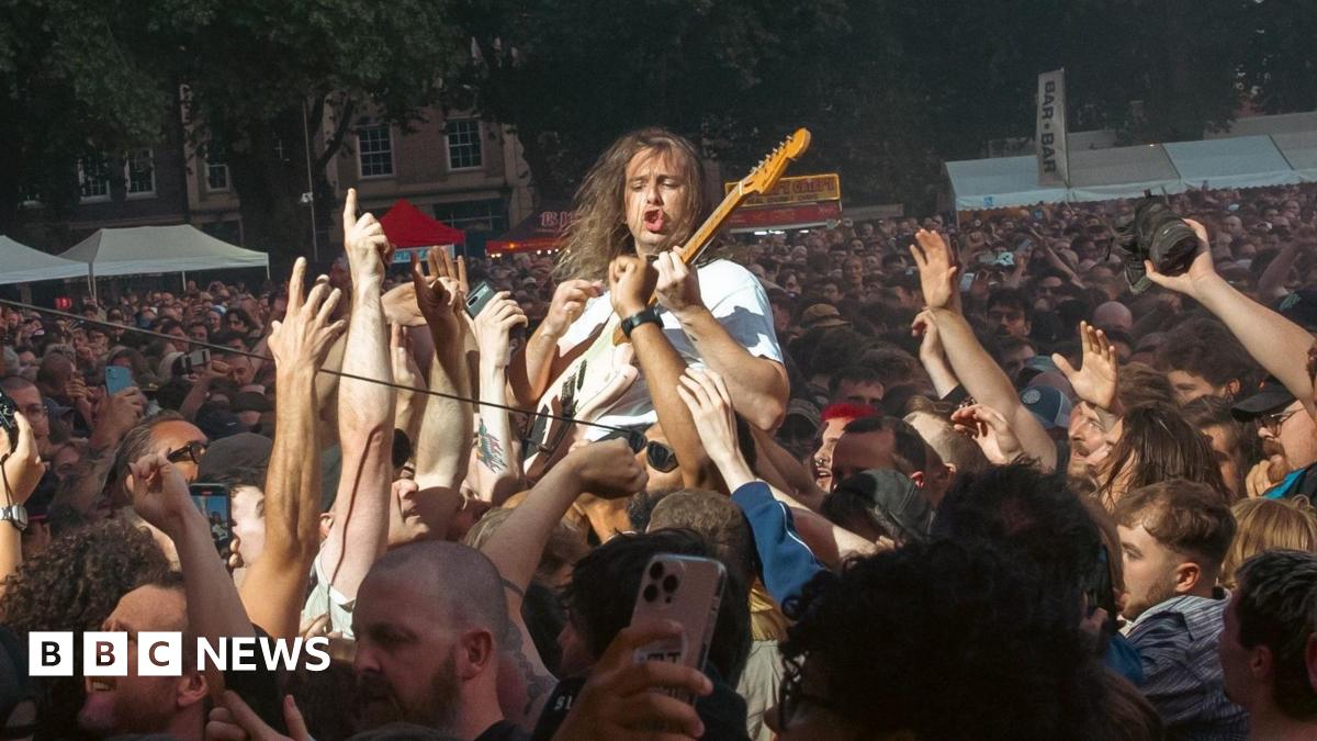 A member of the band Idles is held aloft by the crowd as he plays his guitar during a concert in Queen Square in Bristol. Thousands of people along with food and drink stalls are visible in the background
