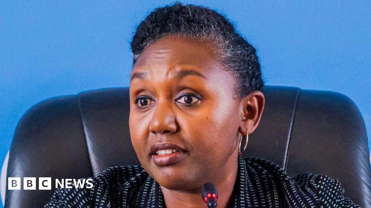 Rwanda government spokesperson Yolande Makole sits on a black chair before a microphone. She is wearing a white dotted black blazer.