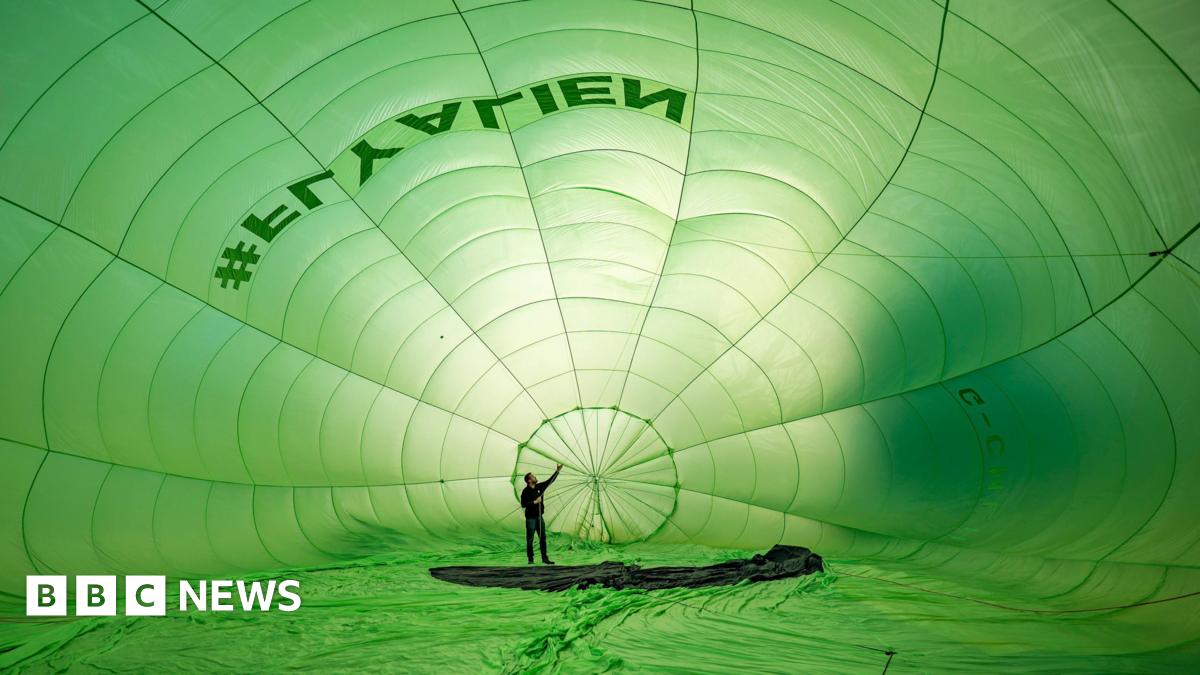 A man is standing in a giant green balloon as it inflates