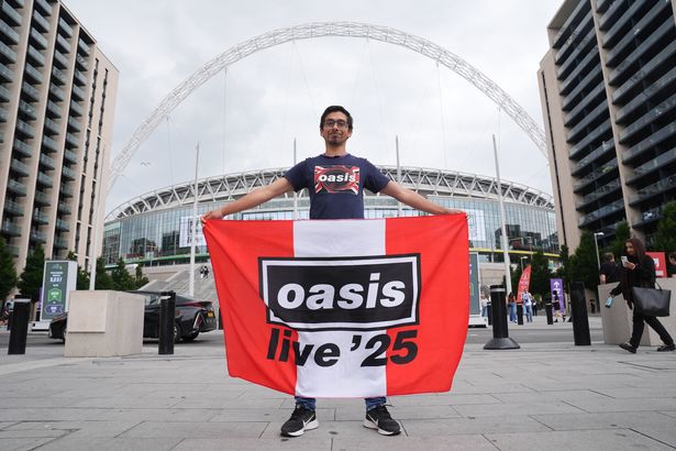 An Oasis fans holds a flag outside the stadium, ahead of the first night of the Oasis Live '25 tour opening at Wembley Stadium
