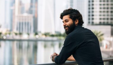 Young man with beard standing outside with a city backdrop, showing quiet wealth and luxury.