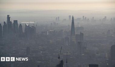 A hazy aerial view of central London, with the Shard and other skyscrapers partially obscured by a haze under a pale sky.