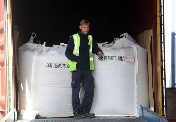 The image shows a man in a high vis jacket standing over a huge bag of peanuts ready to be shipped