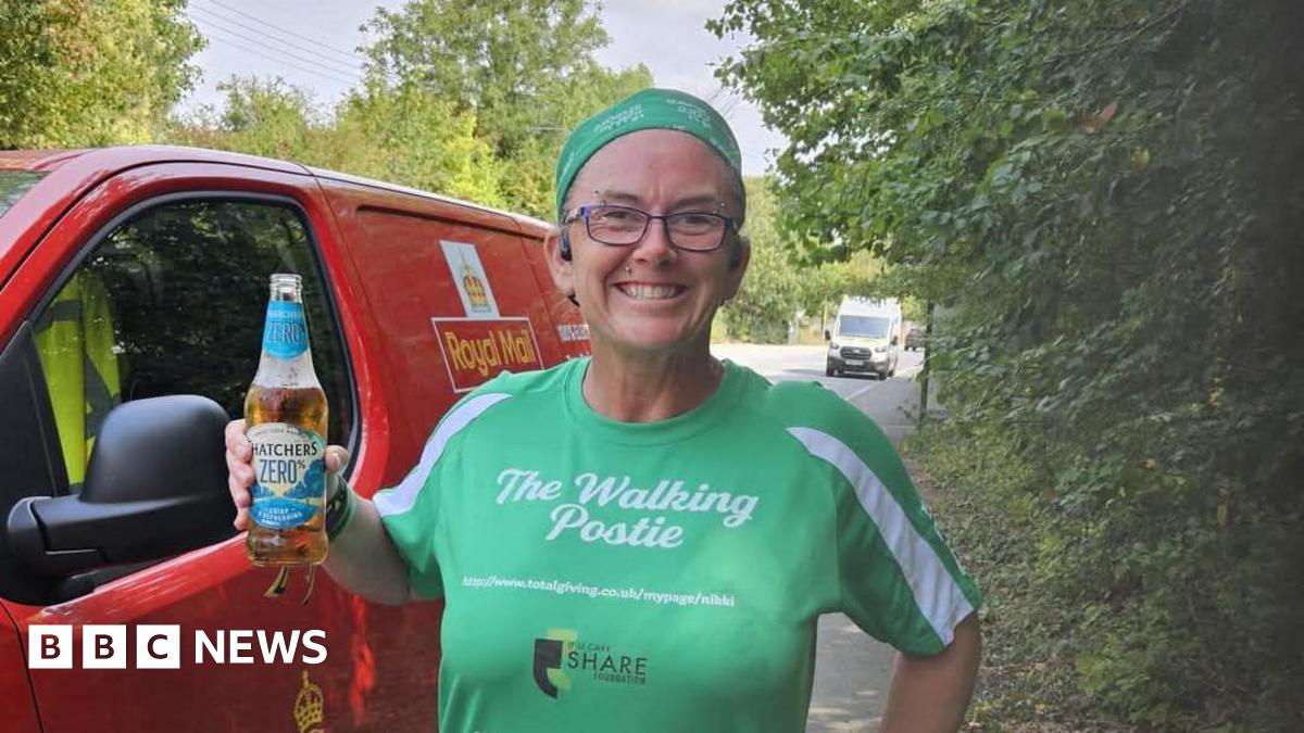 Nikki Gaynor smiling at the camera and stood in front of a Royal Mail van. She is holding a Thatchers Zero bottle in her left hand and is wearing a green shirt which has the words 'The Walking Postie'.