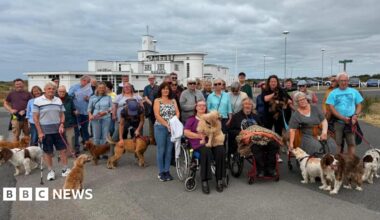 About 30 people, many with dogs, gather on Birkdale Common to protest plans to allow the R&A to take over a section of the public land ahead of the 2026 Open golf championships there. Three people in wheelchairs sit in the foreground, in front of the standing protesters.
