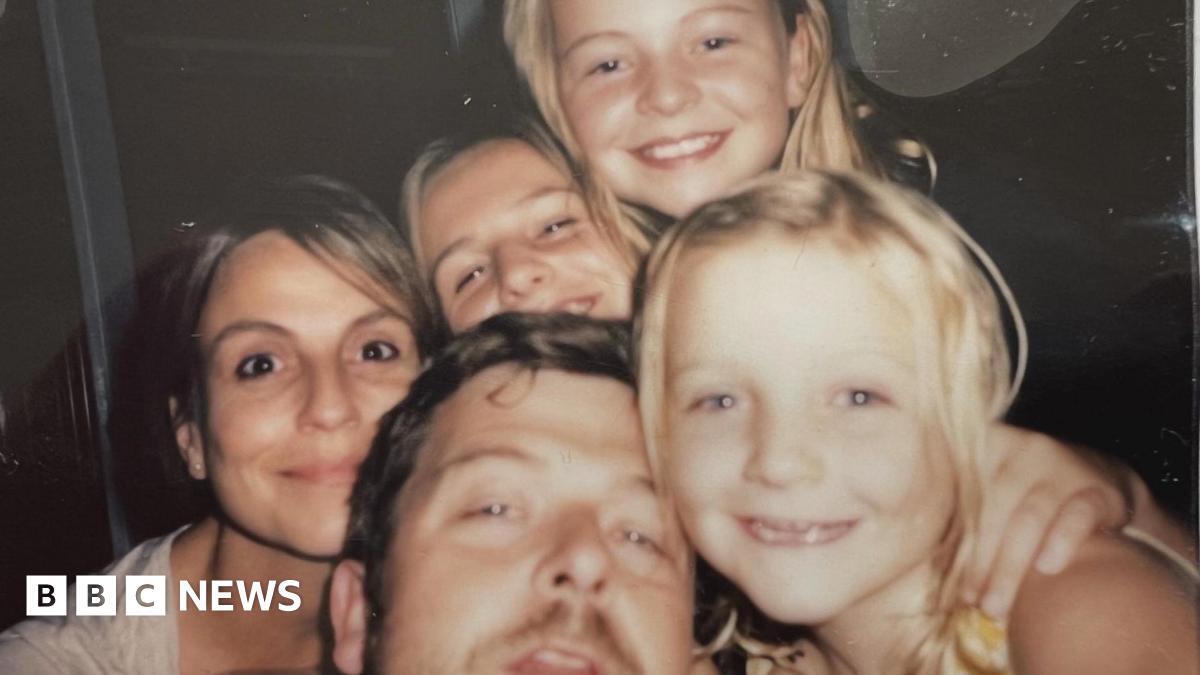 A family photo of the Bastion-Strong family showing Chris and Katie with their three daughters. The family are all close together and smiling as they pose for the picture.