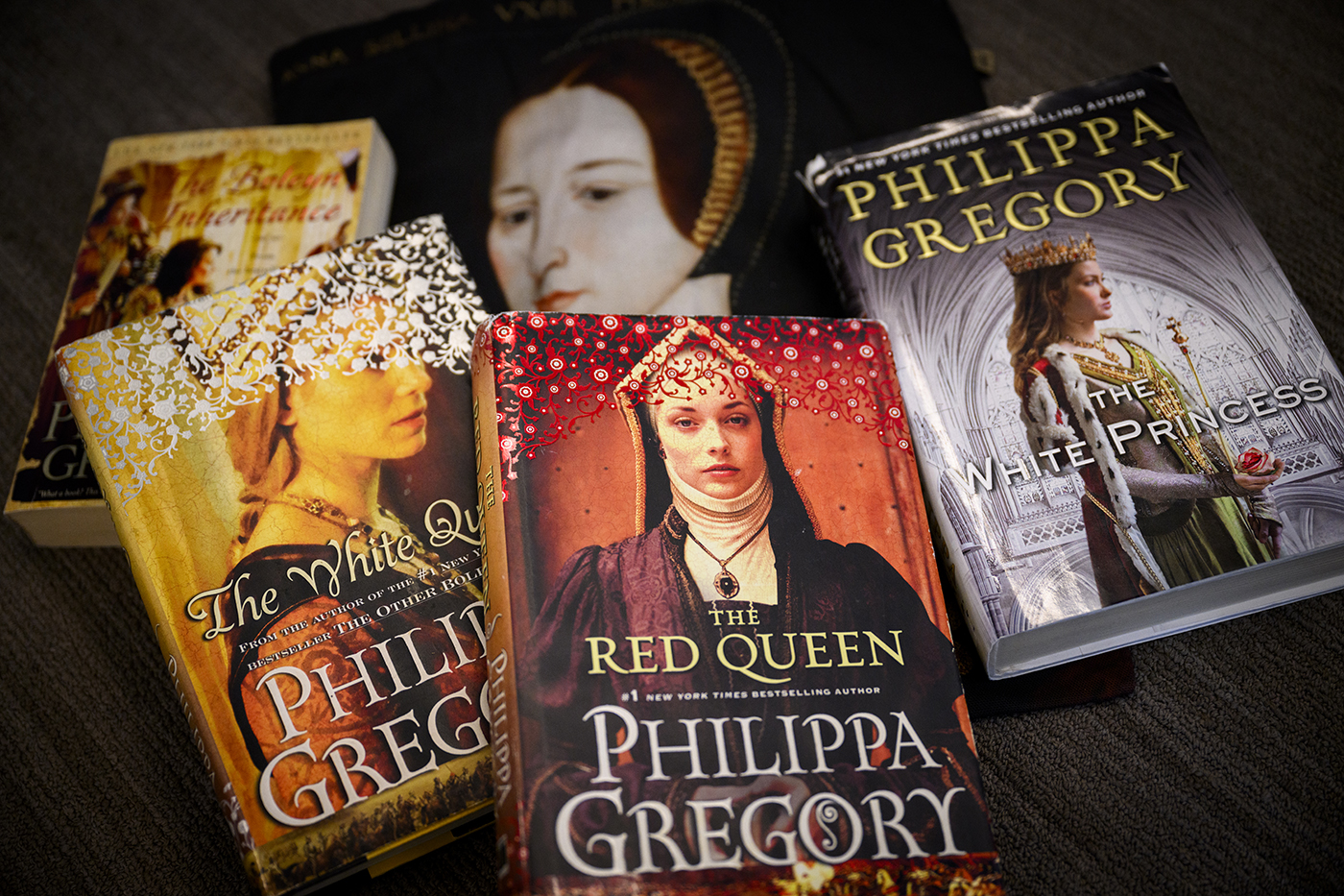 A collection of five Philippa Gregory historical fiction novels displayed on a dark surface. The books shown are 'The White Queen,' 'The Red Queen,' and 'The White Princess,' all part of The Cousins' War series. The book covers feature portraits of women in medieval and Tudor-era clothing and headdresses, with rich colors including gold, red, and purple. The author's name 'PHILIPPA GREGORY' is prominently displayed on each cover.