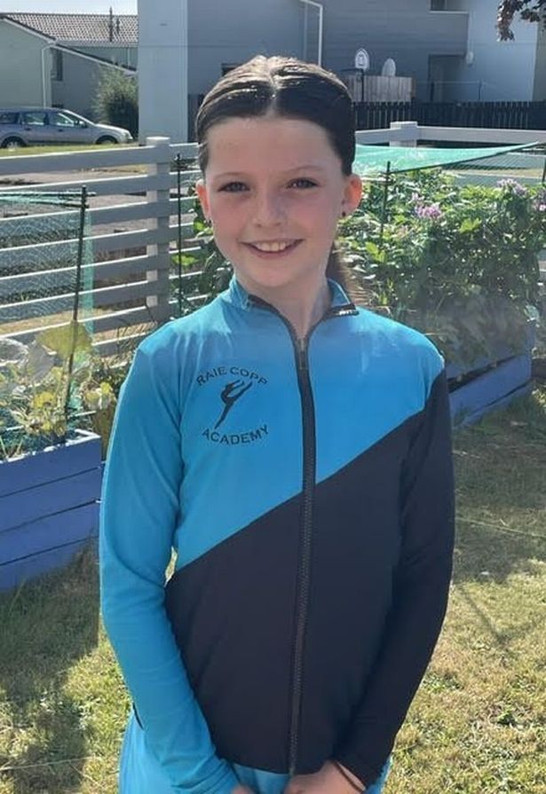 Dakota standing in a garden wearing a RAIE Copp Academy hoodie, smiling in the sunshine