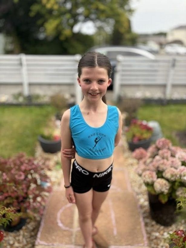 Dakota standing in her garden, with her hands behind her back, smiling
