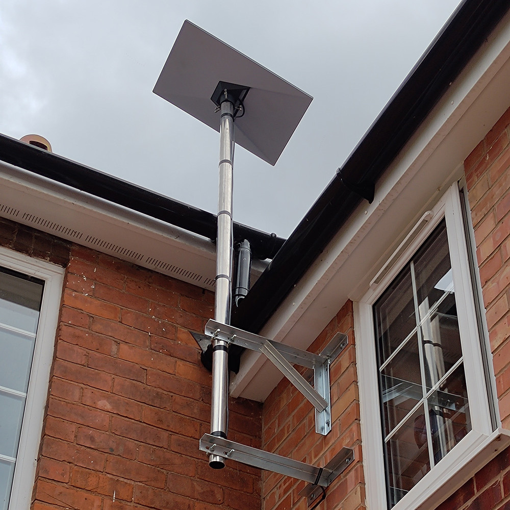 Starlink internet dish mounted by roof on brick wall