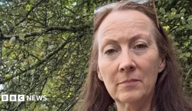 Helen, a small business owner, stands by a tree with her long brown hair blowing in the wind.