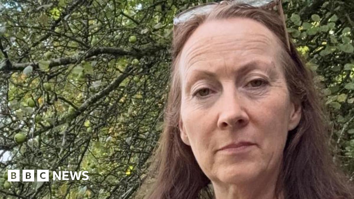 Helen, a small business owner, stands by a tree with her long brown hair blowing in the wind.