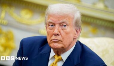 Trump seen in the Oval Office at the White House. He wears a yellow tie and blue suit coat.