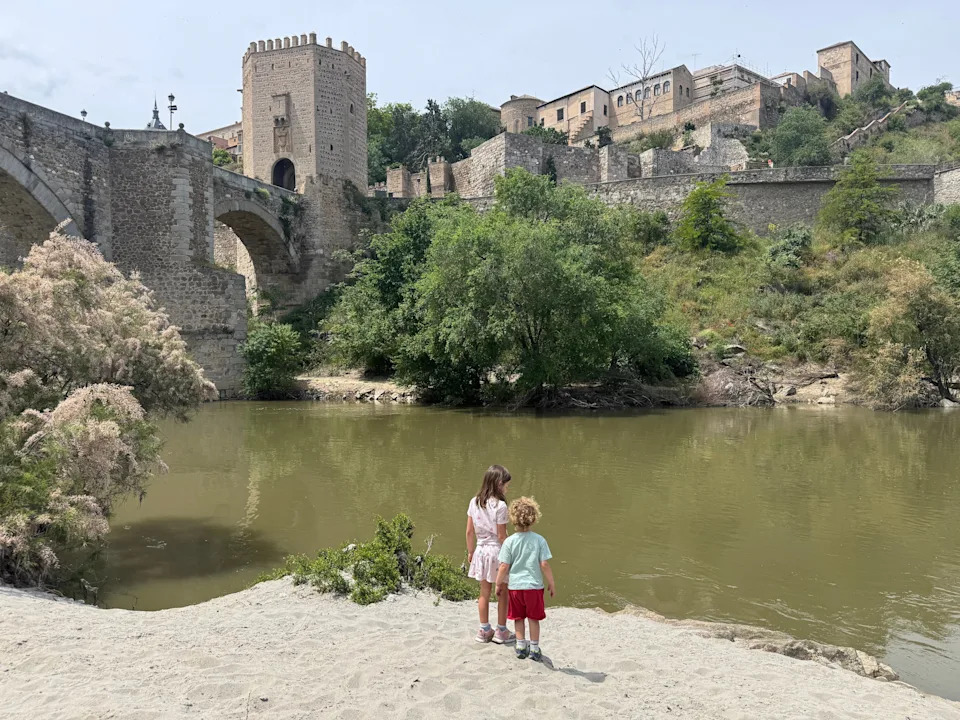 two young children standing on beach in front of spanish city with old style castle