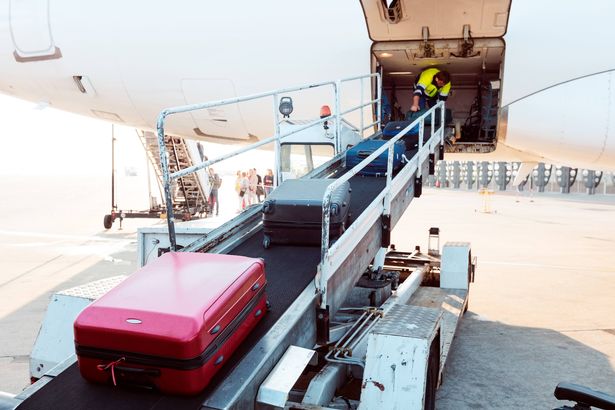 Outdoor shot of young man unloading luggage from airplane. Airport ground crew at work.
