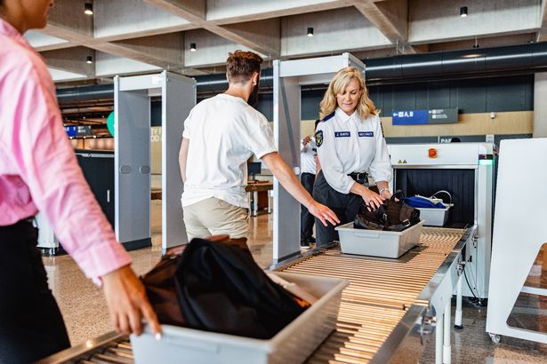 Young adult Caucasian male with a long beard standing next in line to scan his luggage through a x-ray machine at the airport.