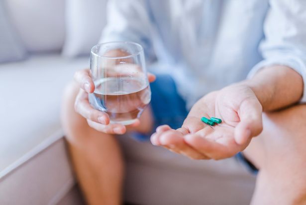 Young man with pill and glass of water at home, closeup.  Young man taking medication, feeling ill. Healthcare concept. Depressed man holds antidepressant meds