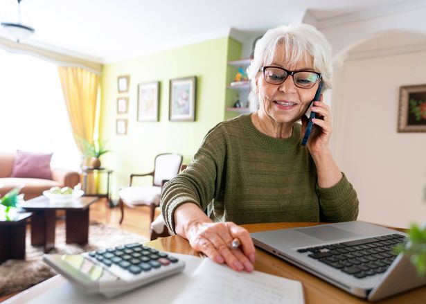 Busy Latin American senior woman talking on the phone working online at home using her laptop