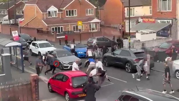 Video grab from terrifying footage shows a machete wielding thugtrying to stab two men after a huge 'Wild West-style' mass brawl erupted on a residential street involving up to 20 people.