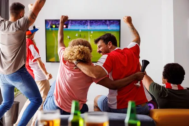 Group of young friends having fun watching football match on TV, drinking beer and cheering