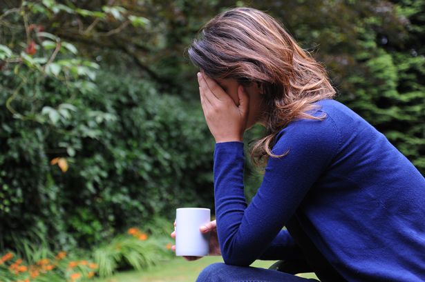 A woman with her head in her hands holding a mug