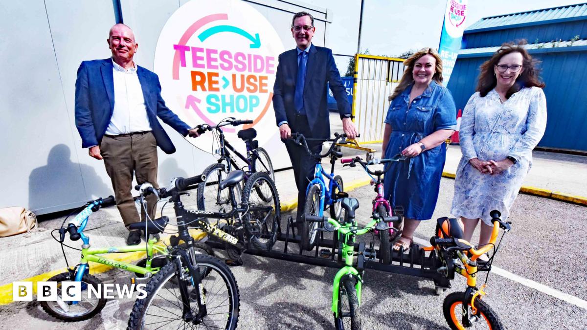 (L-R) Councillor Peter Gavigan, SUEZ Regional Director Steve Patterson, Councillor Lisa Evans and Amanda Padfield, director of public sector development at SUEZ. All four are standing in front of a small bike rack which is supporting seven children's bicycles. A sign on the wall marks the site as the Teesside Reuse Shop.