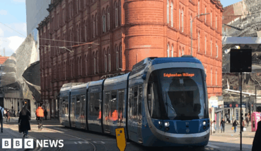 A blue tram on the lines in central Birmingham with a brick building in the background