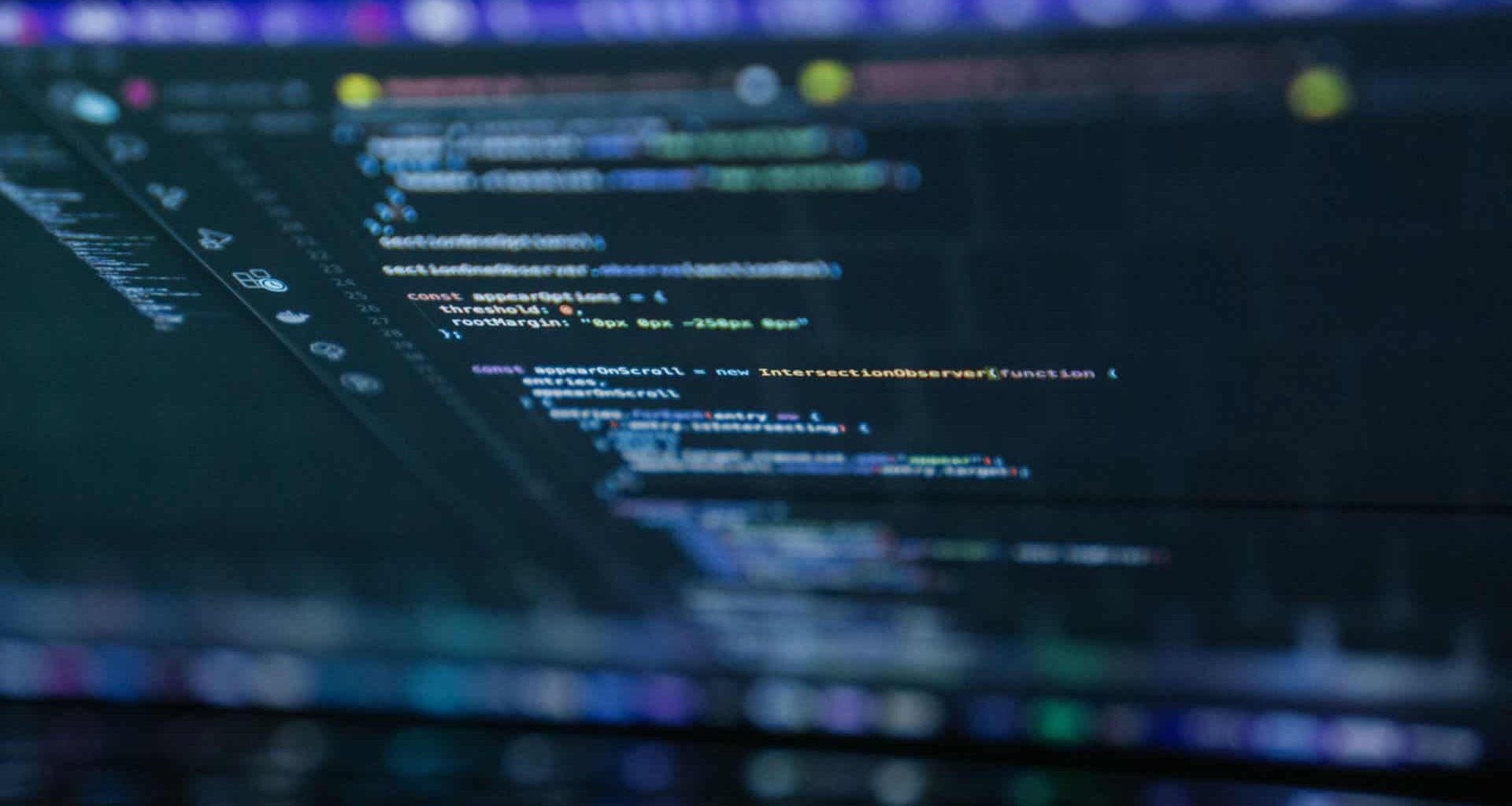 Lines of code on a laptop screen with text highlighted in orange, blue, white, and green on a dark background. Open source