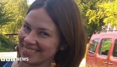 Tetiana Martynova, 40, from Kharkiv, Ukraine, smiles at the camera. She has a short brown bob and brown eyes. Green trees can be seen behind her, as well as part of a red car.