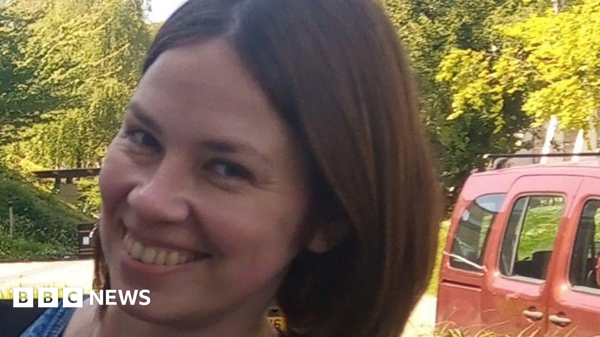 Tetiana Martynova, 40, from Kharkiv, Ukraine, smiles at the camera. She has a short brown bob and brown eyes. Green trees can be seen behind her, as well as part of a red car.