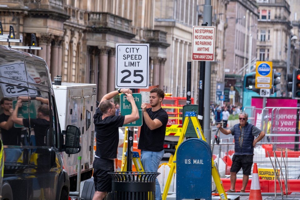 Two men installing a temporary 25 mph speed limit sign on a city street.