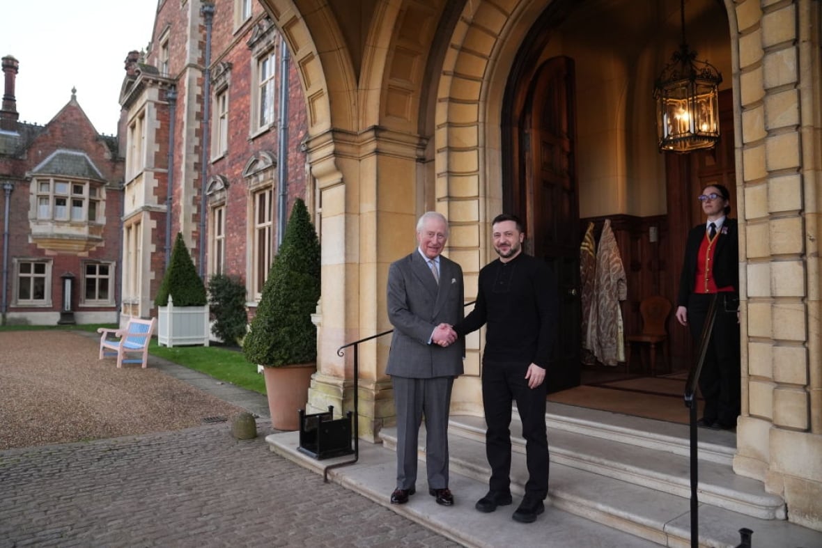 Two people standing on a low step in front of an arched entryway shake hands.