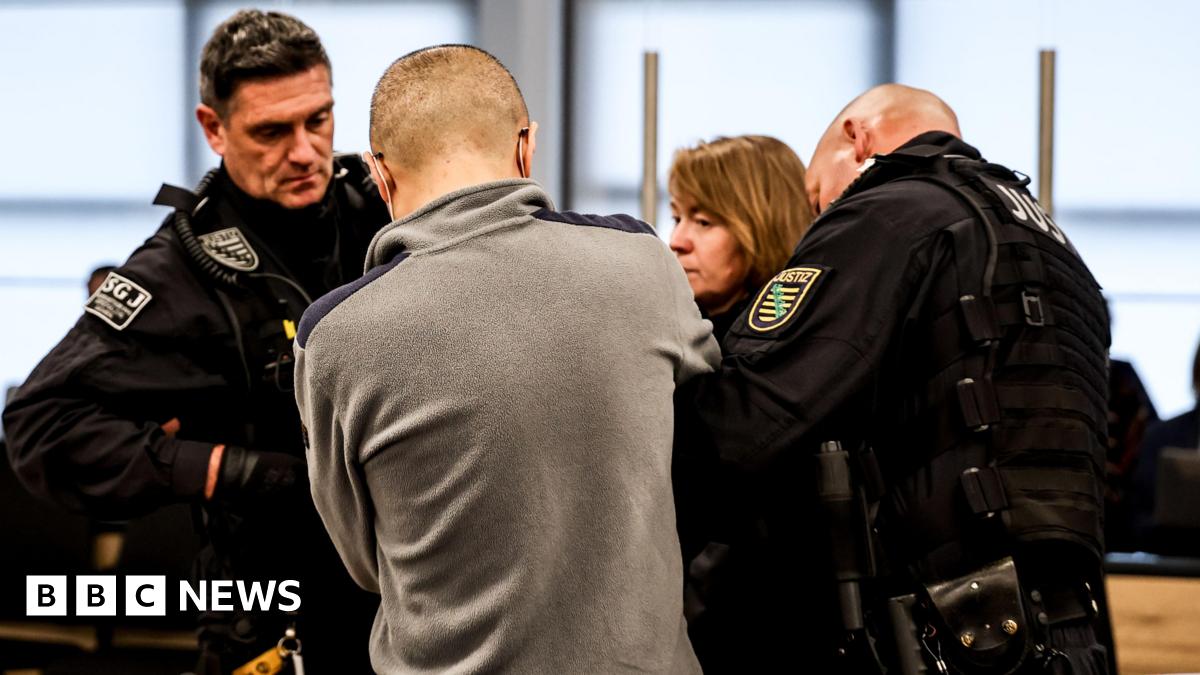 A man is seen from behind standing in front of three prison officers.