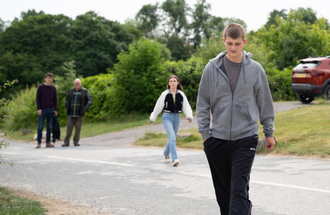 Dylan Penders walking away from April Windsor in the Emmerdale village, as Marlon Dingle and Paddy Kirk watch in the distance.