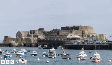 A view of Castle Cornet on an island with a number of small boats on the water in front of it.