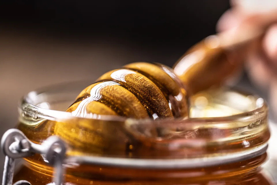Honey dripping from honey dipper in glass jar.  Healthy organic Thick honey dipping from the wooden honey spoon, closeup.