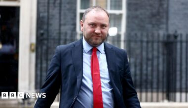 Ian Murray looking straight at the camera. He is wearing a blue suit over a light blue shirt with a red tie. He is standing in front of the front of 10 Downing Street.