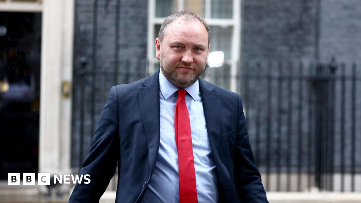 Ian Murray looking straight at the camera. He is wearing a blue suit over a light blue shirt with a red tie. He is standing in front of the front of 10 Downing Street.