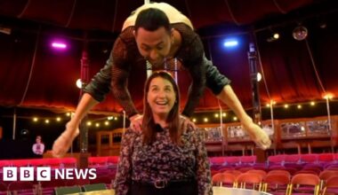 Circus perfomer balancing with his hands on the shoulder of BBC reporter