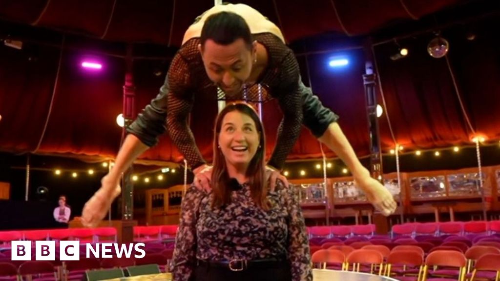 Circus perfomer balancing with his hands on the shoulder of BBC reporter